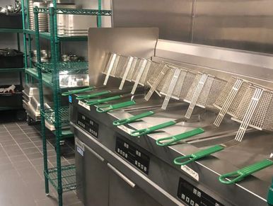 Row of deep fryers with green-handled baskets in a commercial kitchen.