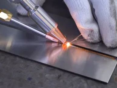 Close-up of a gloved hand performing precision welding on metal sheets.