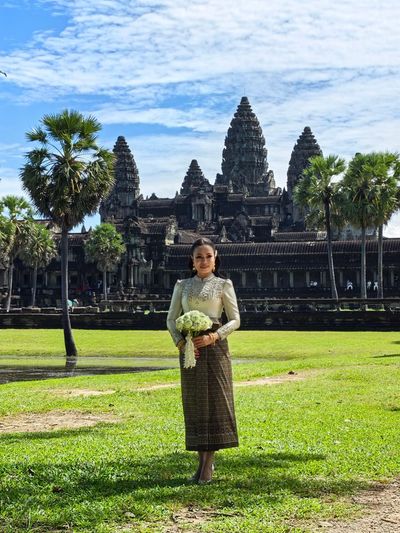 A woman in traditional attire holding flowers in front of Angkor Wat.