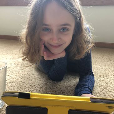 Young person lying on carpet using a yellow tablet.