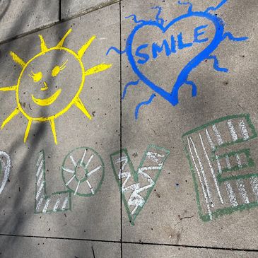 Chalk drawings of a sun, heart with 'SMILE', and word 'LOVE' on sidewalk.