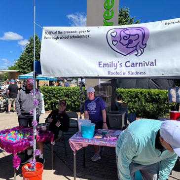 Volunteers at Emily's Carnival fundraiser booth on a sunny day.