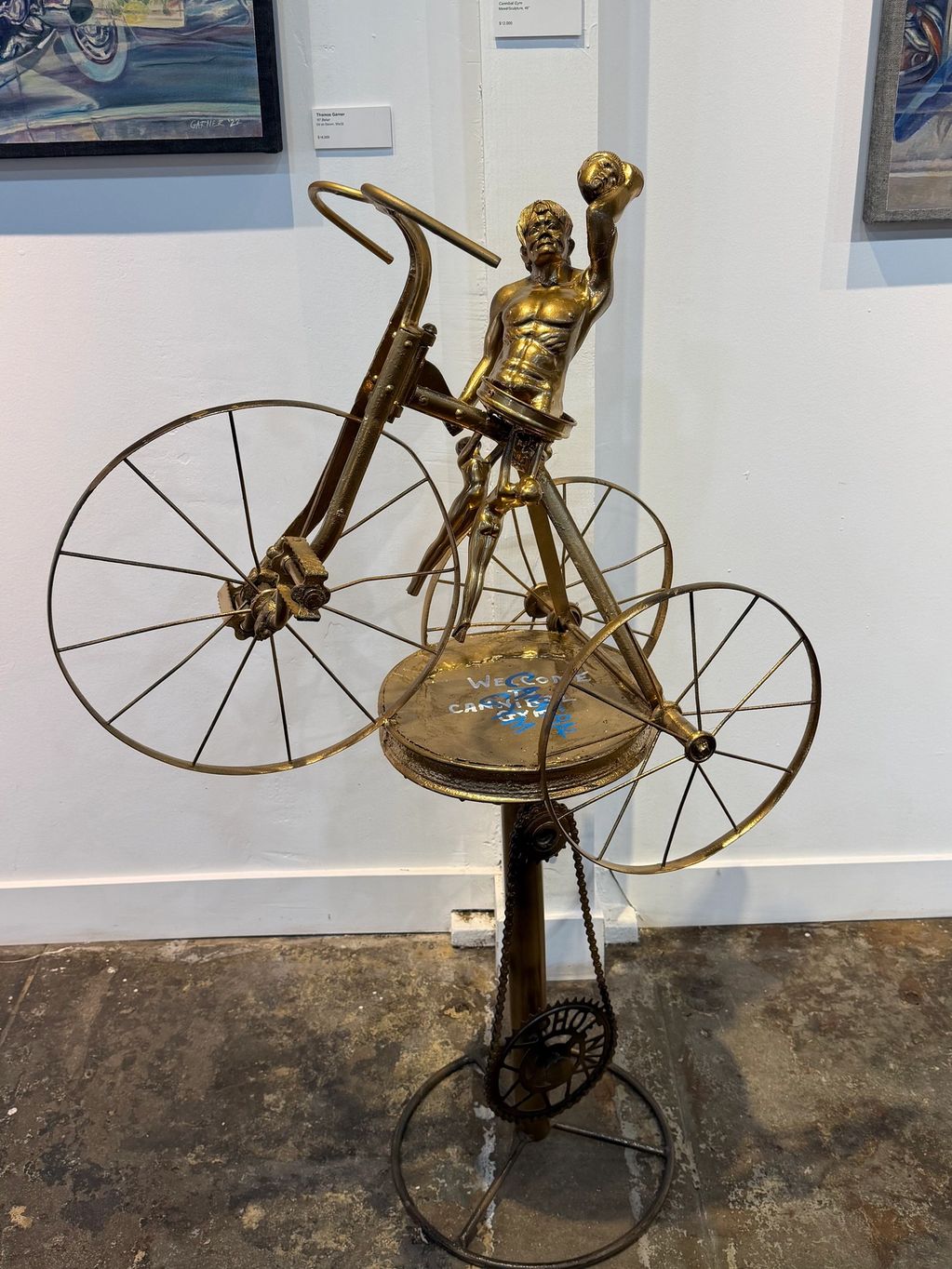 A golden sculpture of a man holding a ball on a vintage bicycle.
