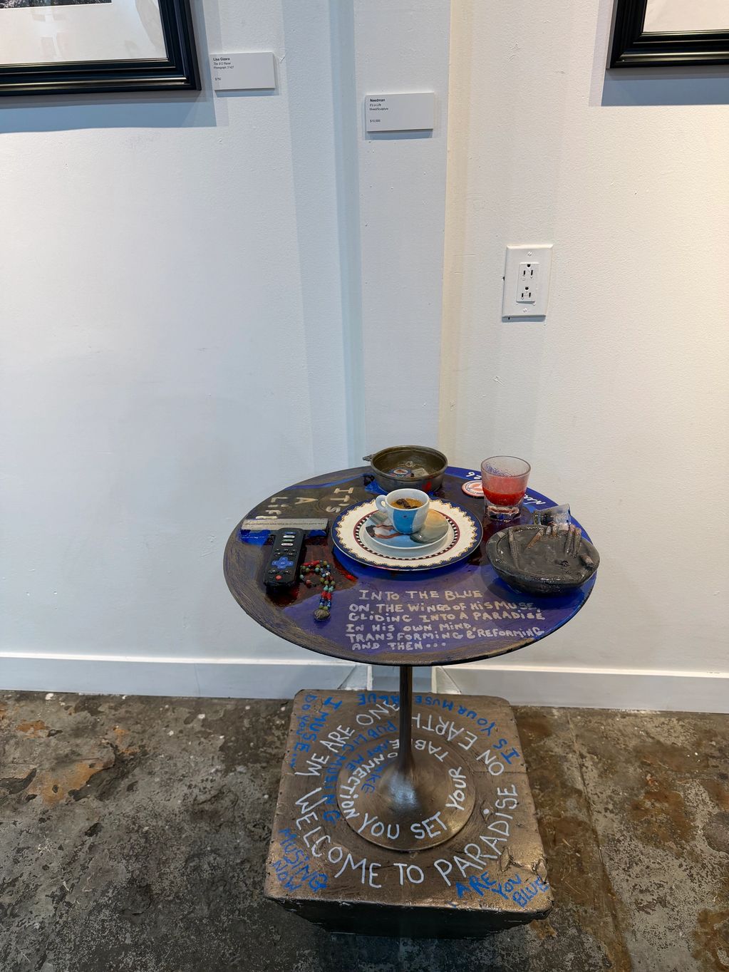 Artistic table display with coffee, glass, remote, and handwritten messages on the surface and base.