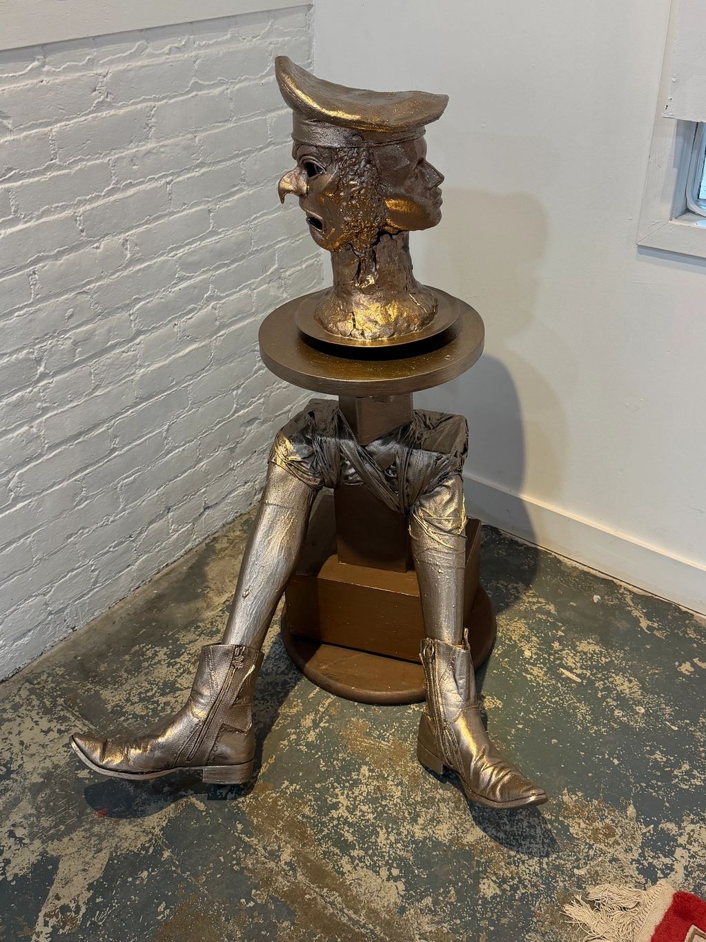 A bronze sculpture with a multi-faced head and metallic legs wearing boots.
