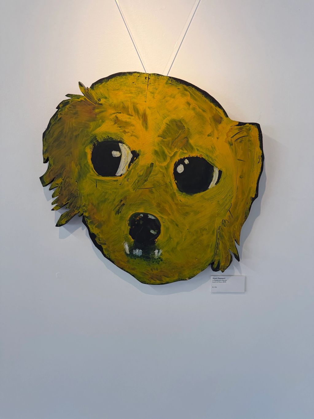 Abstract yellow dog face painting hung on a white wall.