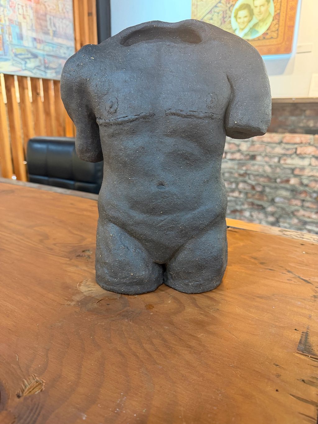 A black torso sculpture without head and arms on a wooden table.