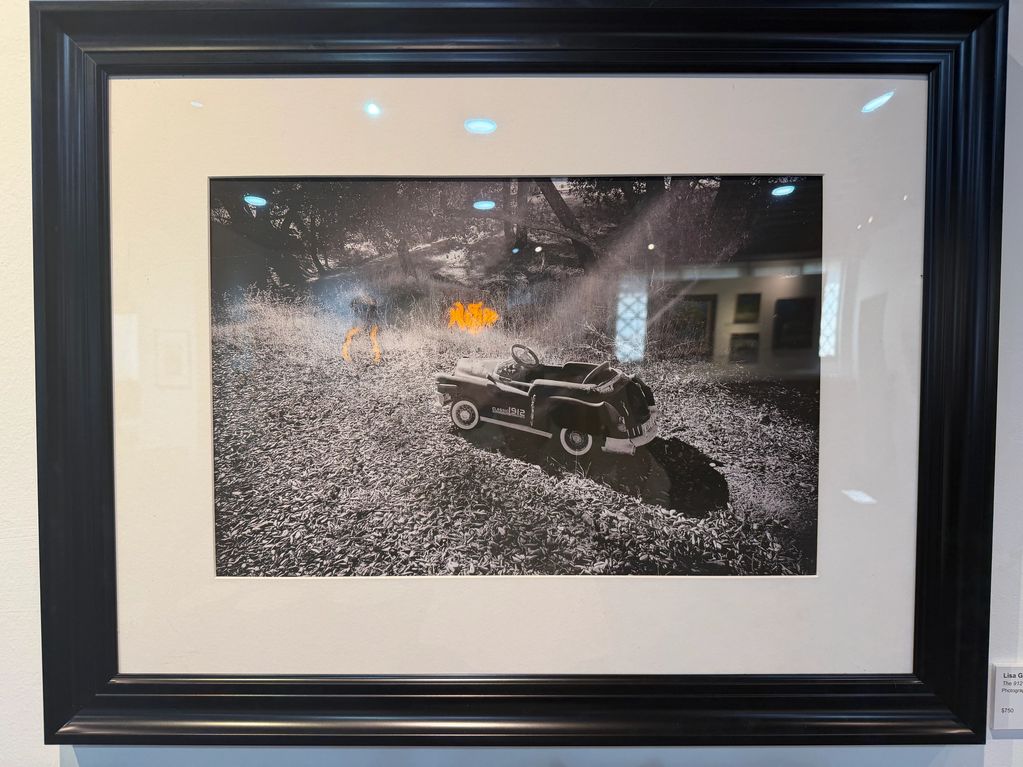 Black and white photo of a toy car in leaves with an orange dog in the background.