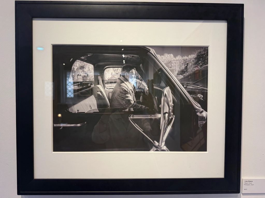 Black and white photo of a man sitting inside a truck, captured through the window.