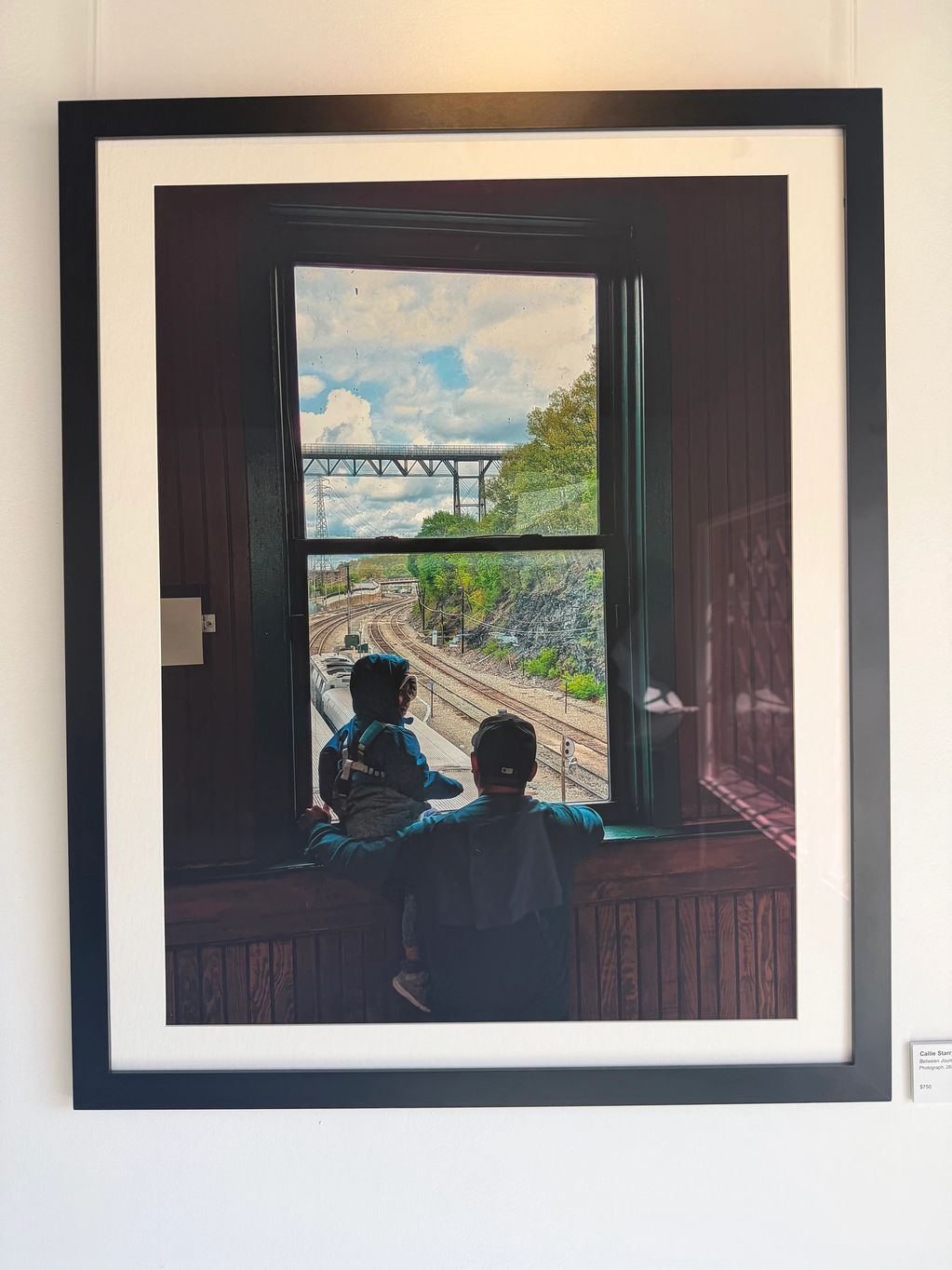 A man and child look out a train station window at railway tracks.