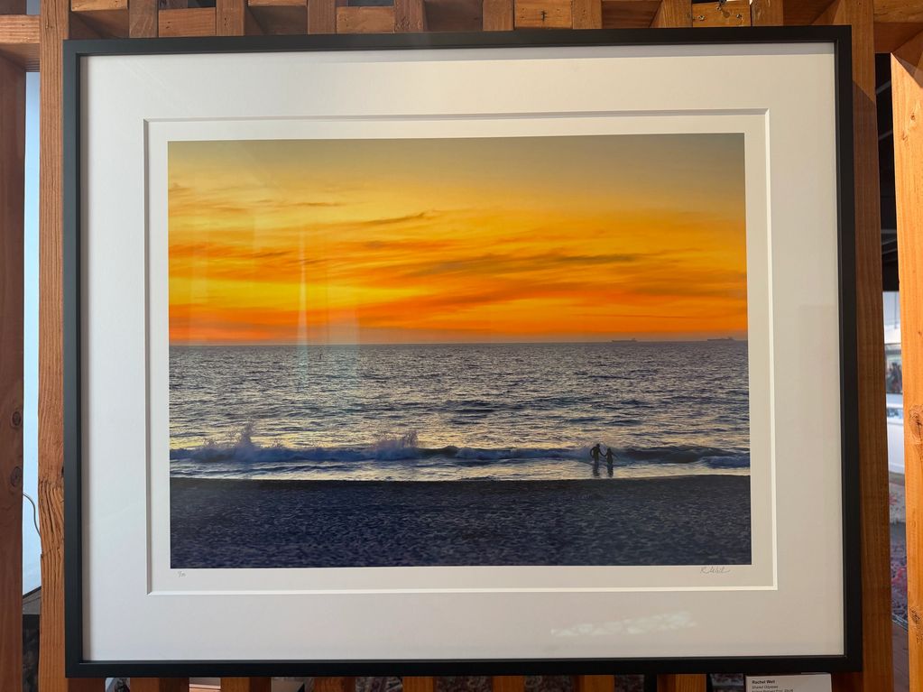 Framed photograph of a sunset at the beach with two people near the water.