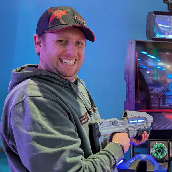 Man smiling while holding a futuristic toy gun in an arcade.