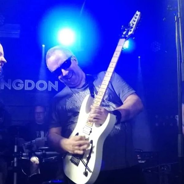 Man passionately playing an electric guitar on stage with blue lighting.