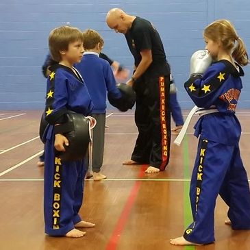 Two children in blue kickboxing uniforms facing each other during training.
