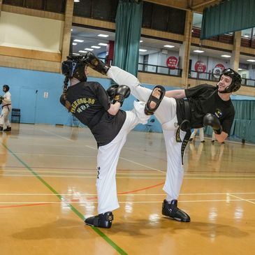Two martial artists sparring indoors wearing protective gear.