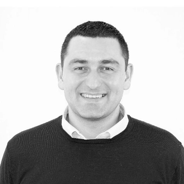 Smiling man in a black sweater over a collared shirt against a white background.