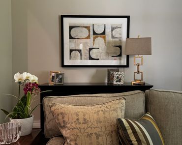 Cozy living room corner with cushions, plants, and modern art.