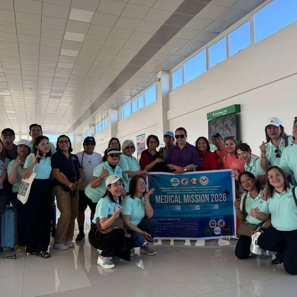 Group photo of medical mission team holding a banner at an airport terminal.