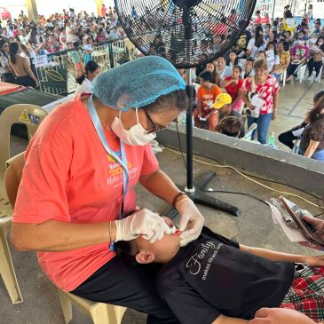 Healthcare worker performs dental checkup on a child in a crowded community event.