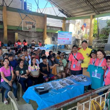 Community gathering in a covered basketball court with health info and giveaways.