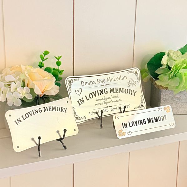 Three memorial plaques with flowers on a white shelf.