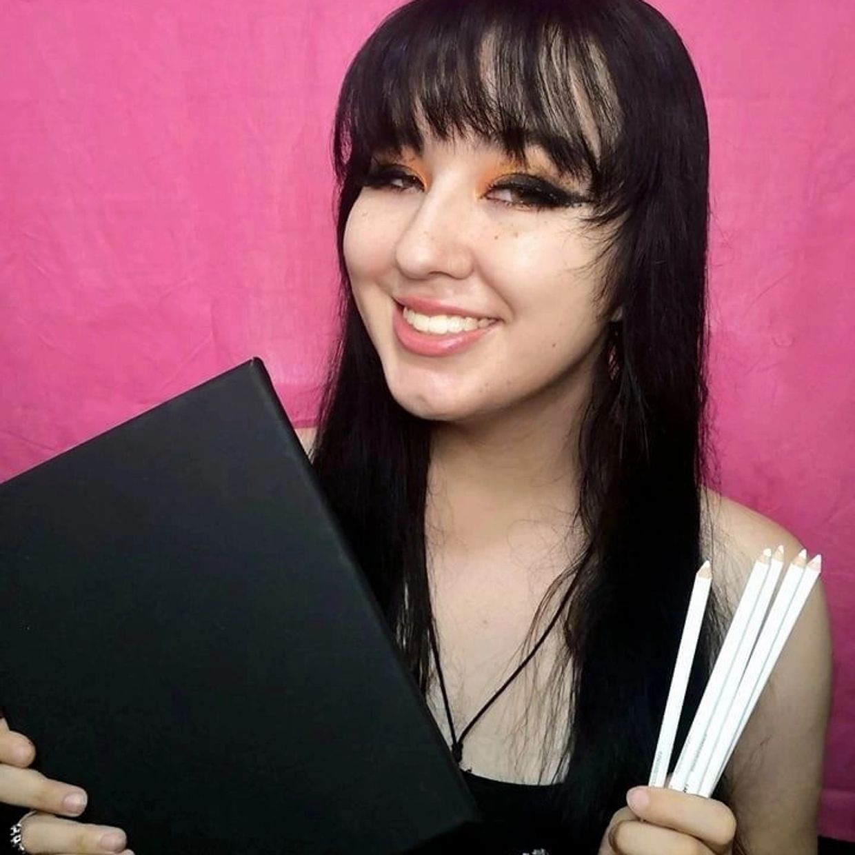 Autumn Szabo posing with a black canvas and colored pencils in front  of a pink background