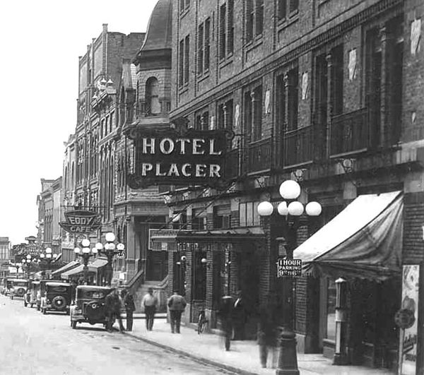 Historic black and white street scene with Hotel Placer and vintage cars.