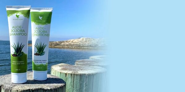 To flasker Aloe-Jojoba shampoo og balsam ved sjøen.