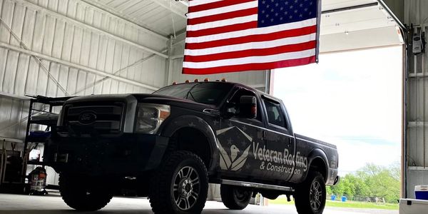 A black Veteran Roofing truck parked inside a garage with an American flag.
