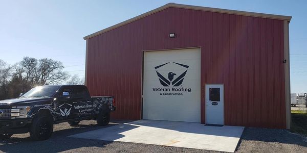 A red building and black truck with Veteran Roofing branding.