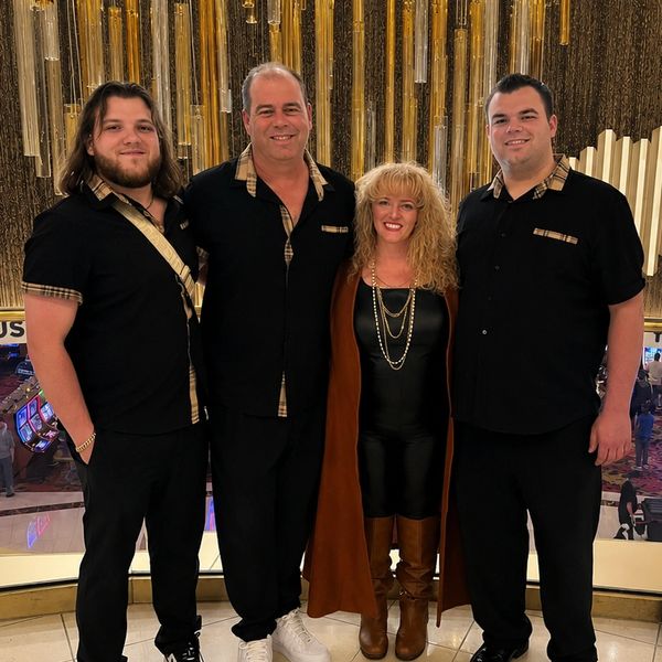 Group of three men and one woman posing in a stylish indoor setting.