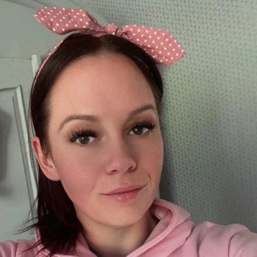 Young woman with pink polka dot headband and pink hoodie smiling slightly.