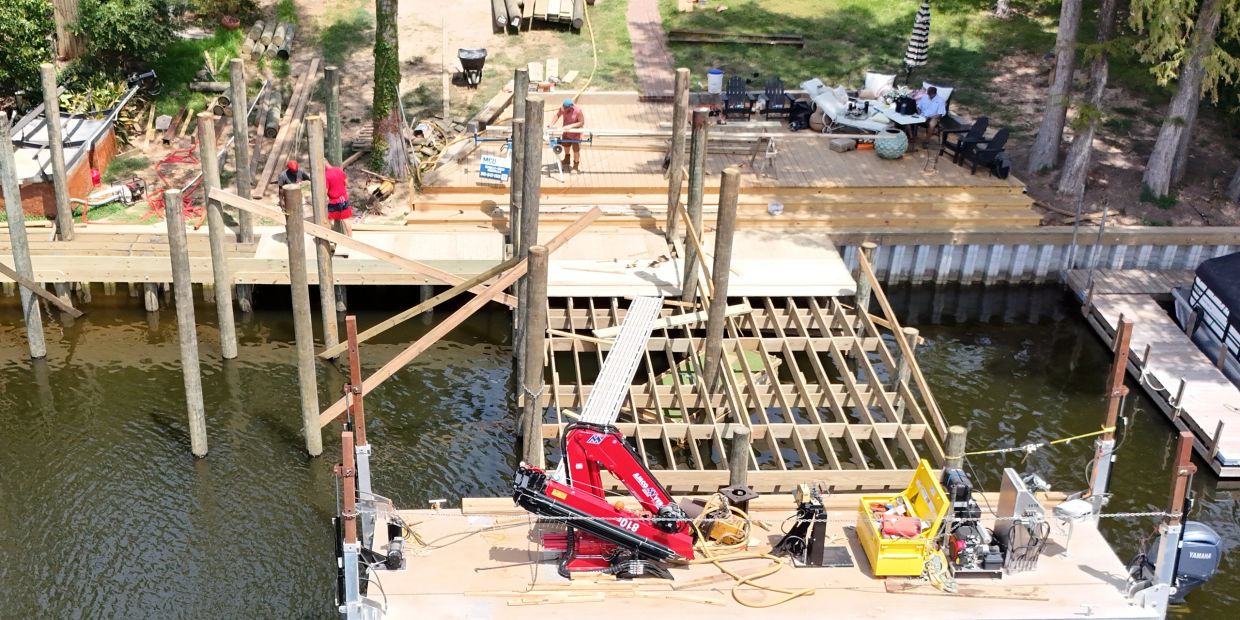 Construction of a wooden dock over water with workers present.