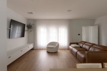 Modern living room with leather sofa and round white chair by sheer curtains.