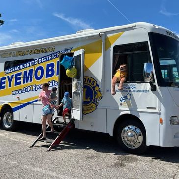 Children entering a mobile eye screening bus on a sunny day.