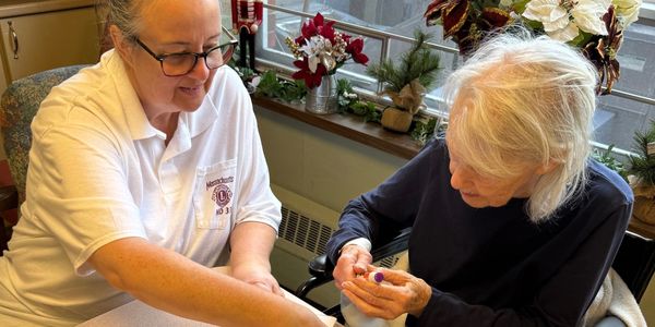 Caregiver assists elderly woman with a task at a decorated table.