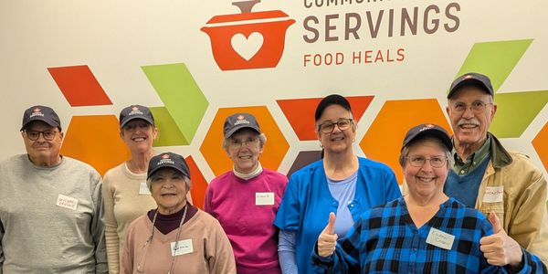 A group of smiling volunteers posing in front of a food help organization sign.