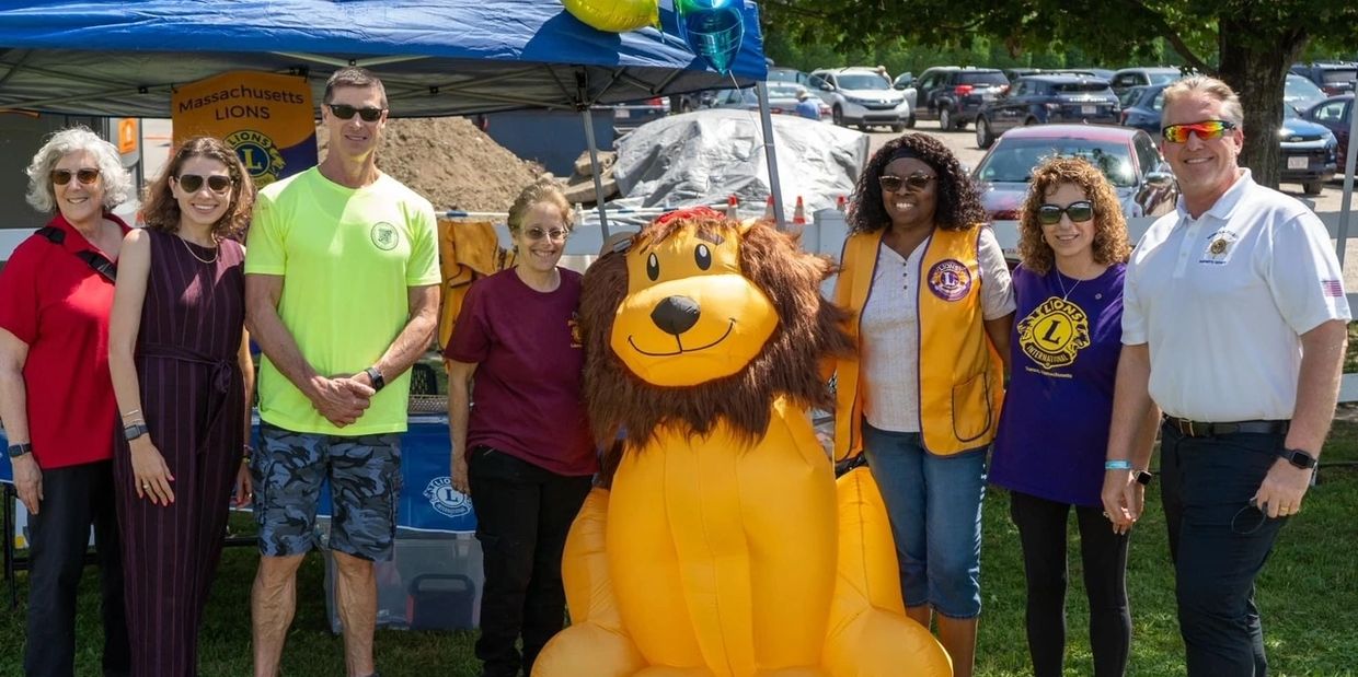 Group of people posing with a large inflatable lion mascot at a Massachusetts Lions event.