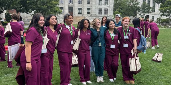 Group of students in medical scrubs posing outdoors on a university campus.
