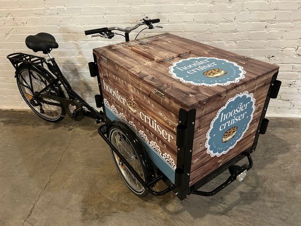 A black tricycle with a wooden cargo box labeled "hoosier cruiser."