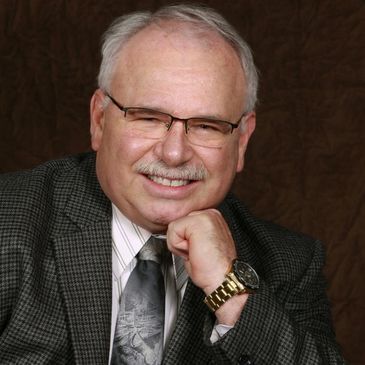 Smiling elderly man with glasses and a suit.