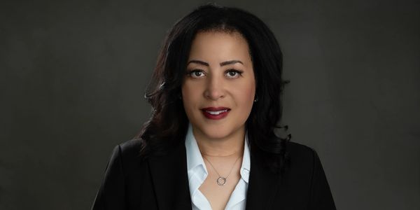 Professional woman in black blazer and white shirt with elegant necklace.