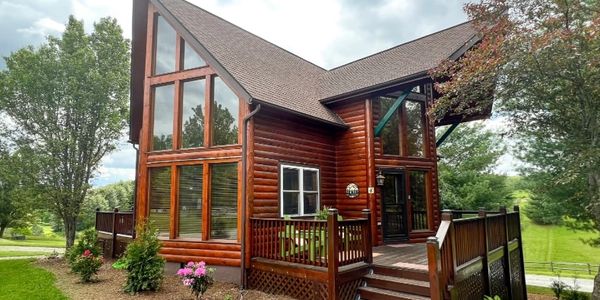 Cozy log cabin with large windows and a wooden deck in a green landscape.