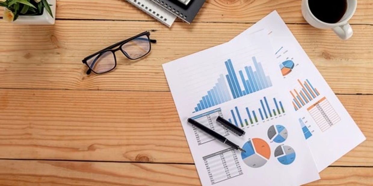 Workspace with charts, glasses, calculator, and coffee on wooden table.