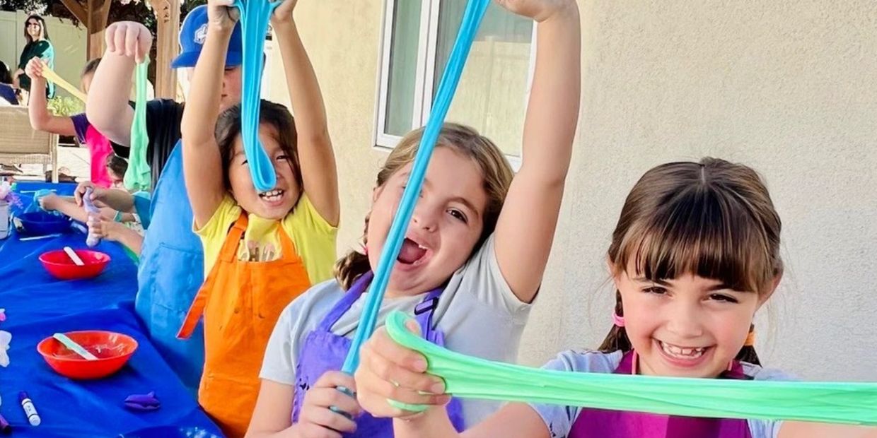 Kids happily playing with colorful slime at a craft table.