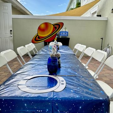 Outdoor space-themed party setup with starry tablecloth and planet decorations.