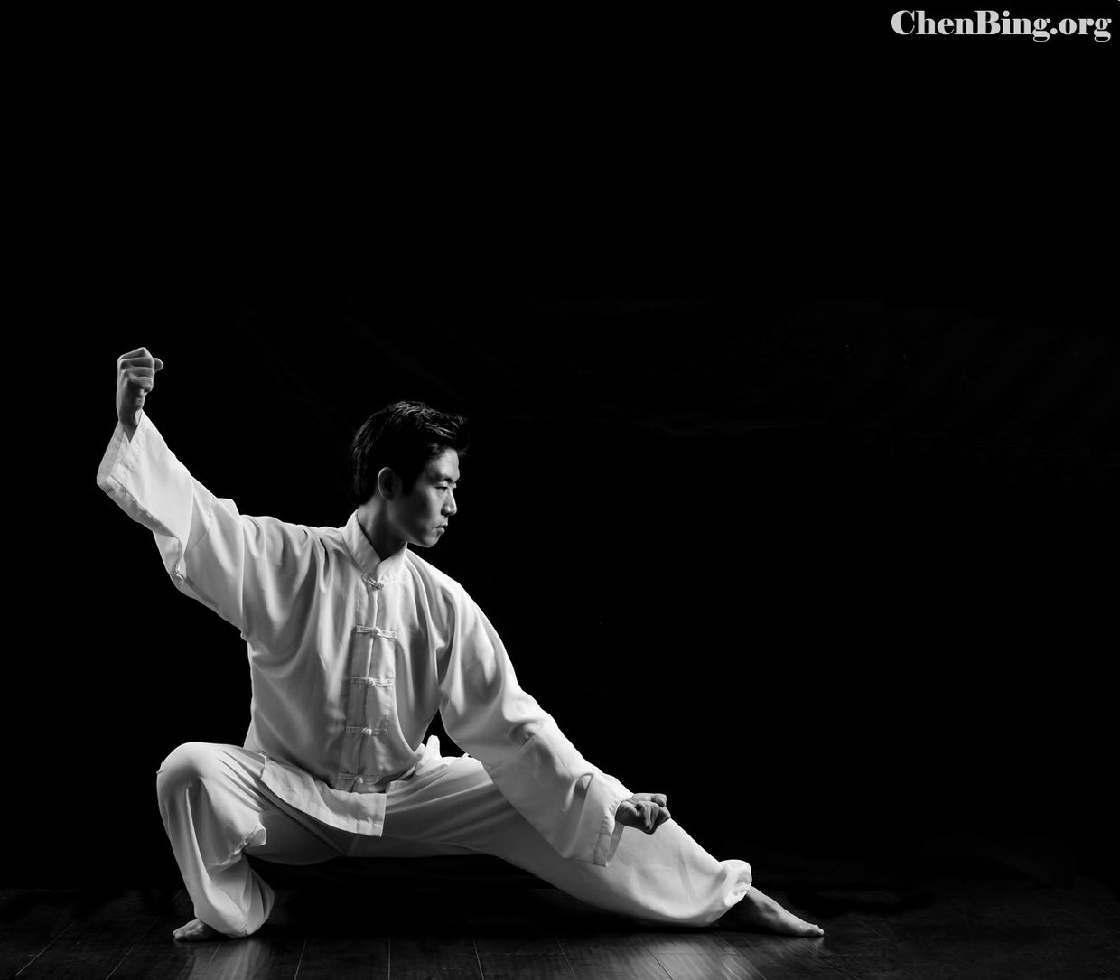 Man practicing martial arts in white attire against a black background.