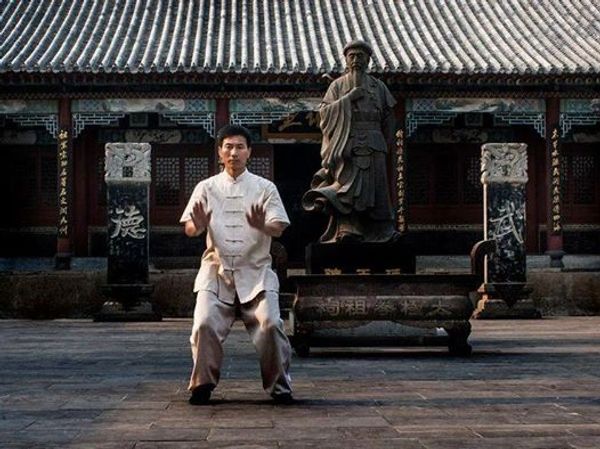 Man practicing martial arts in front of a statue.