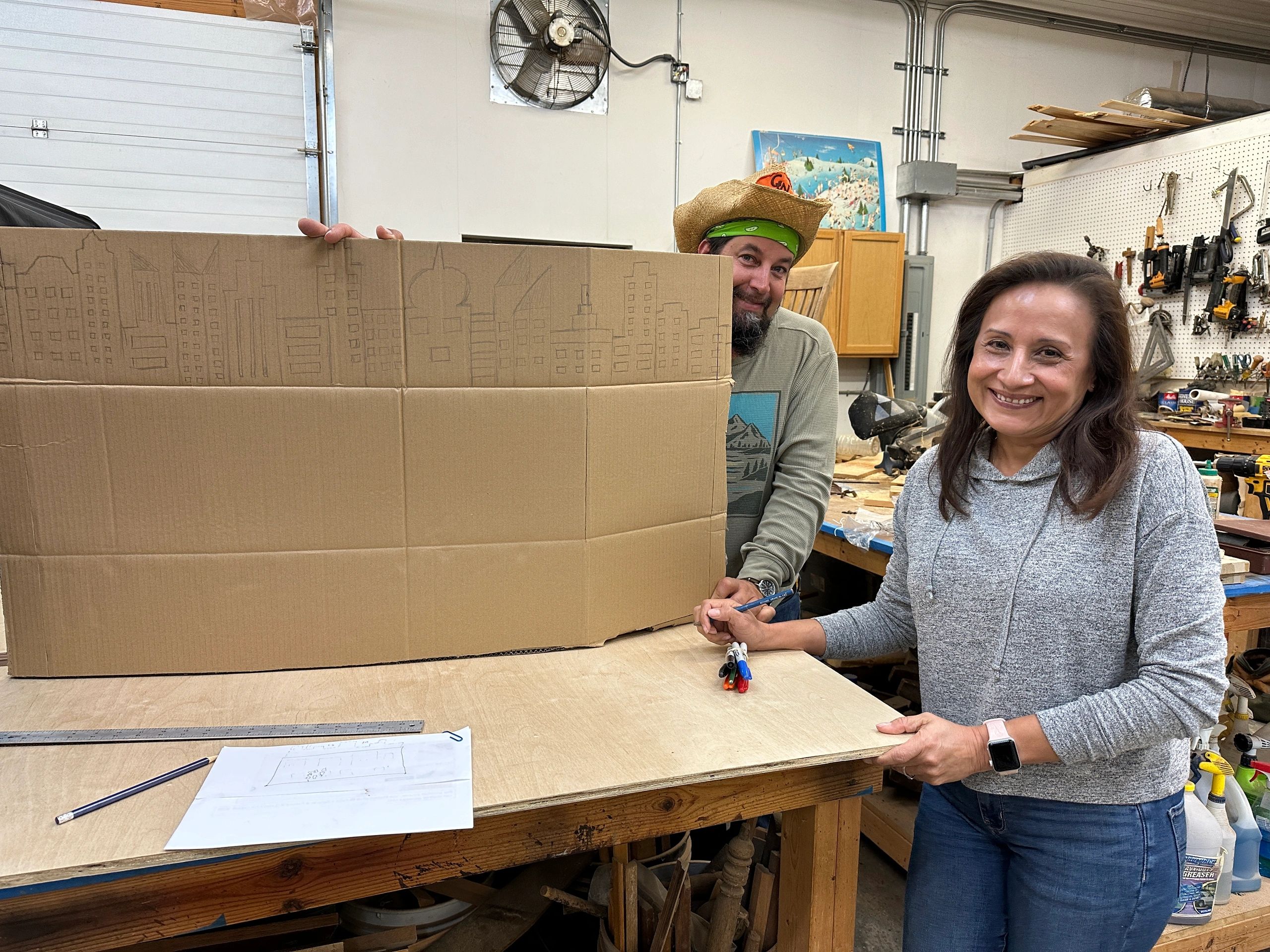 Two EGG volunteers, a smiling man and woman in a workshop, create hands-on materials for the Earth D