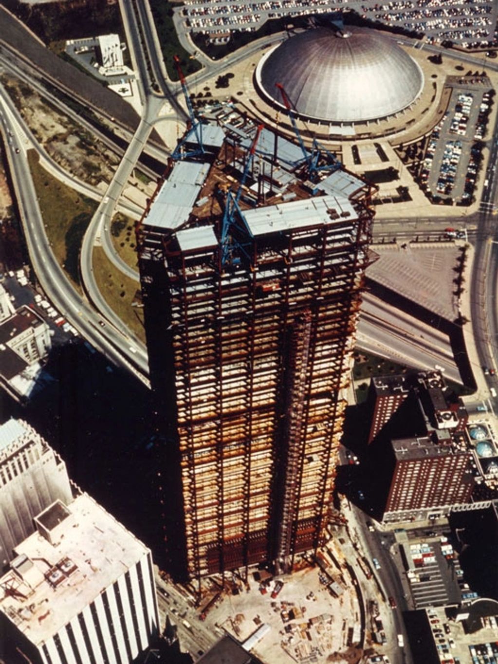 Aerial view of a skyscraper under construction near a domed stadium.